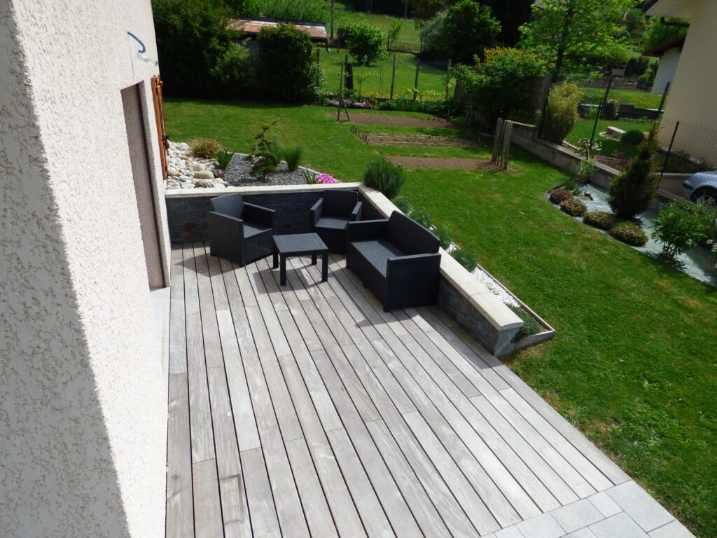 aménagement d'un salon d'extérieur cosy avec une terrasse en bois, un mur de soutènement et un massif végétal